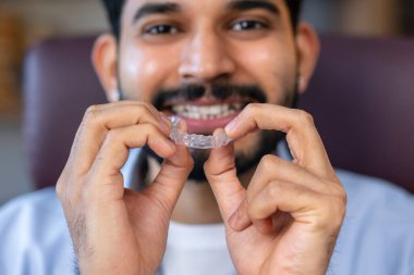 Adamın biri diş düzeltmesi için görünmez silikon hizalayıcı gösteriyor. Dişleri düzeltmek için plastik diş tellerini tutan erkek eller.