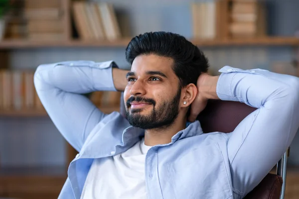 Cheerful Arab Freelancer Guy Leaning Back In Chair, Relaxing After Successful Work, Sitting At Table With Laptop Computer In Home Office, Millennial Man Resting At Workplace With Hands Behind Head