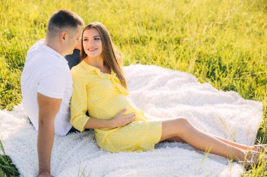 Hamile bir genç kadın yürürken kocasıyla birlikte bir tarlada oturur. Doğada yürü.