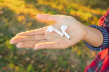 Female Palm 'daki kablosuz kulaklıklar yeşil arka planda izole edildi. Beyaz Parlak Kablosuz Bluetooth kulaklıklar. Koşu için kablosuz kulaklık. Yakın plan.