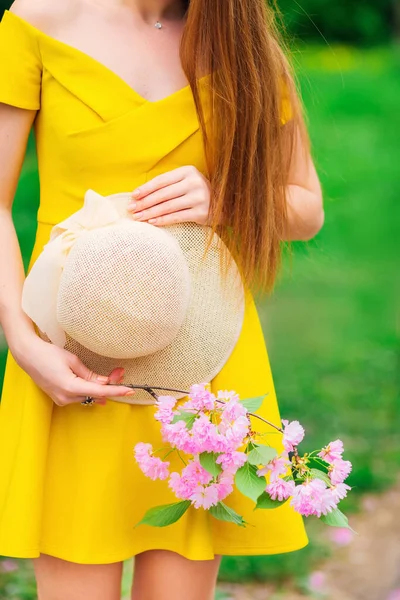 Dziewczyna Żółtej Sukience Gołym Ramieniem Gospodarstwa Kapelusz Gałązka Różowymi Kwiatami — Zdjęcie stockowe