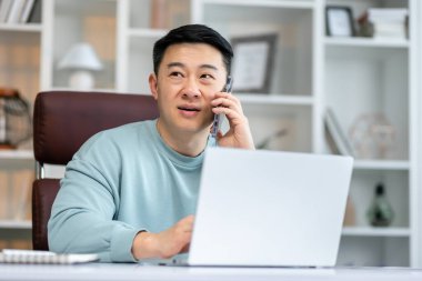 Adam telefonda konuşuyor, dizüstü bilgisayarla masada oturuyor, arkadaş canlısı yönetici müşteriye telefonla danışıyor.