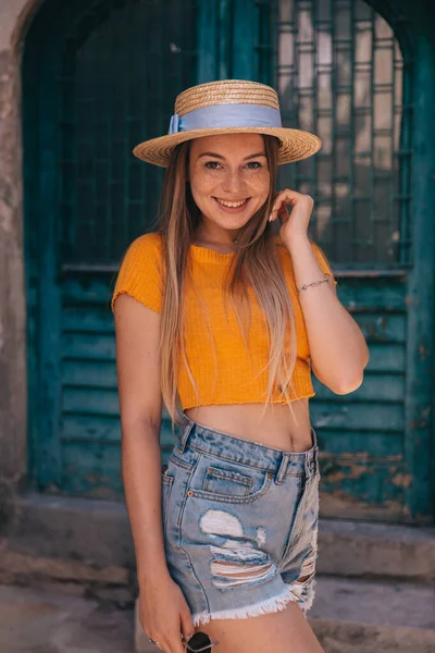 若いです魅力的なスタイリッシュな女性で黄色のTシャツとわら帽子を背景色の良いドアの上にポーズ — ストック写真