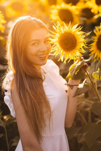 可爱而快乐的年轻女子站在镜头前 将黄色的向日葵放在她的脸上 向日葵地中央的雌性模特儿孤身一人 — 图库照片