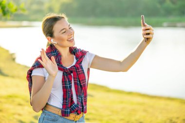 Parkta akıllı telefon kullanarak video araması yaparken mutlu gülümseyen genç bir kadın. Çevrimiçi görüntülü arama yapan el sallayan kız