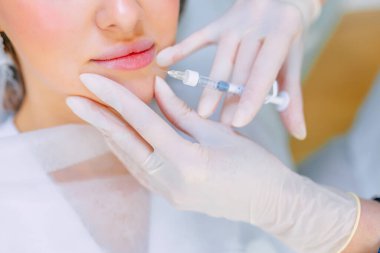 Bir kozmetoloji salonunda dudak büyütme ve düzeltme prosedürü. Uzman hastanın dudaklarına iğne yapıyor.