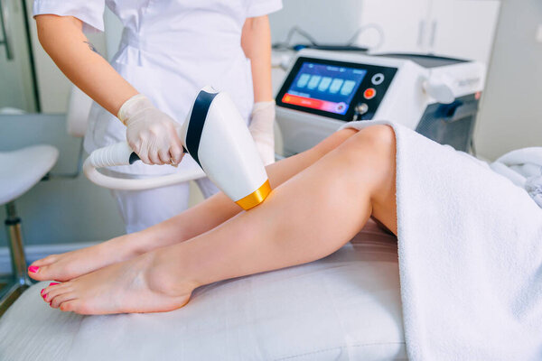beautician removes hair on beautiful female legs with a high-quality laser device.