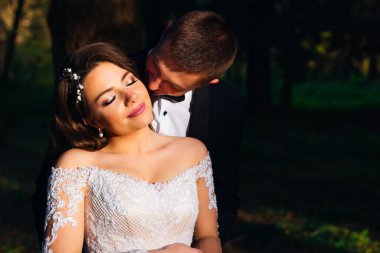 Gelin ve damat kucaklaşıyor. Güzel makyajlı gelin gözlerini kapadı ve damat onu yanağından öpmek istiyor. Kapat. 