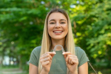 Happy young woman is holding an invisalign bracer clipart