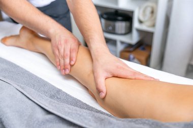 Masaj terapistinin elleri masaj salonundaki genç bayanın bacaklarına masaj yapıyor.