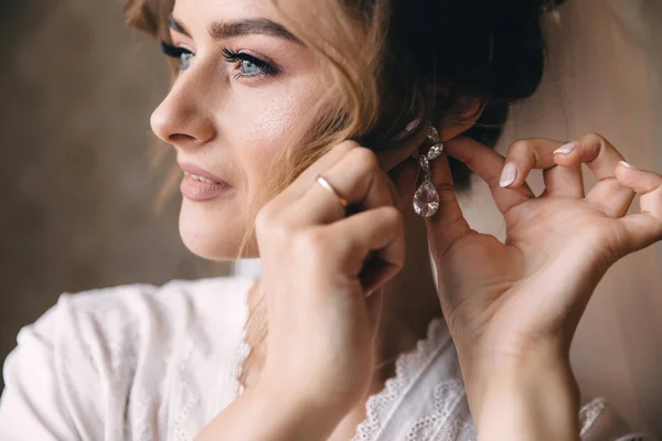 一位漂亮的新娘在早晨的准备工作中戴上一只金耳环 手放在耳朵上 — 图库照片