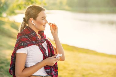 Yan görüşlü kız kulağına kulaklık takıyor ve müzik dinlemek ya da sokakta iletişim kurmak için kulaklıkları açıyor. Bir kutuda kablosuz modern kulaklıklar