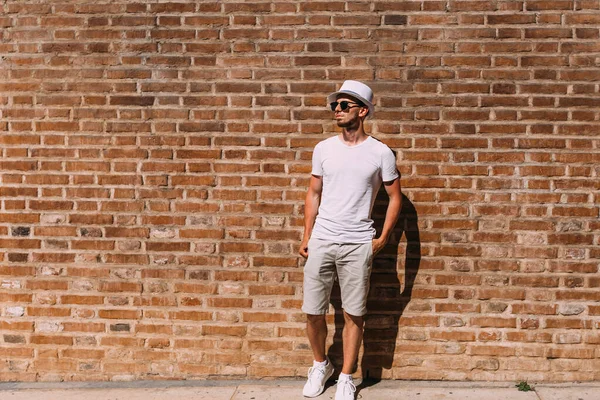 Beyaz Elbiseli Güneş Gözlüklü Bir Adam Tuğla Duvarın Yanındaki Ceplerde — Stok fotoğraf