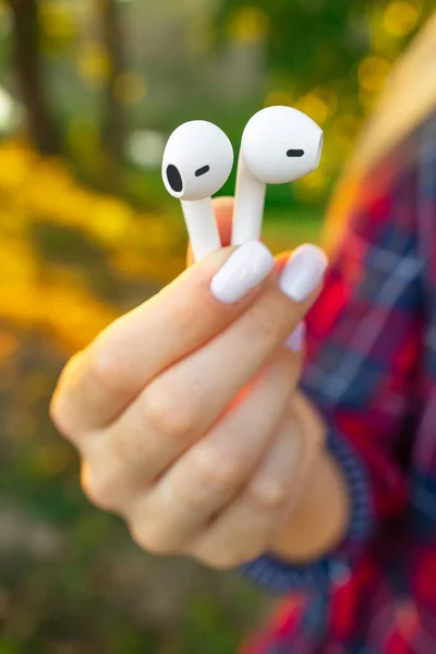 Female Fingers Holds Wireless Earbuds outdoors. Close-up view.