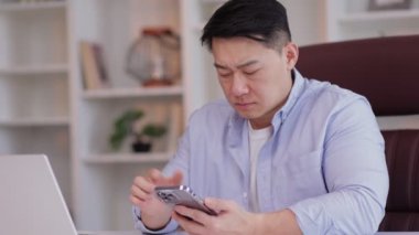 Ofisteki Asyalı iş adamı akıllı telefon kullanıyor. Veri girilemiyor. Zayıf bir internet ağı yok. Erkek kullanıcı, akıllı telefon uygulamasında kötü haber servisinden dolayı hayal kırıklığına uğradı 