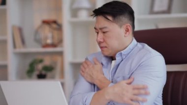 Asyalı işadamı ofiste dizüstü bilgisayarla çalışırken üşüyor ve titriyor, klimayı kapatıyor. Ofis çalışanı iş yerinde oturuyor ve ev sıcaklığı düşük..