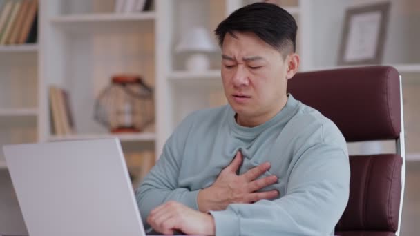 アジアのビジネスマンは突然彼のオフィスでラップトップで働く彼の胸に触れ 急性心痛を感じ 心臓発作の危険性 プロの燃え尽きる — ストック動画