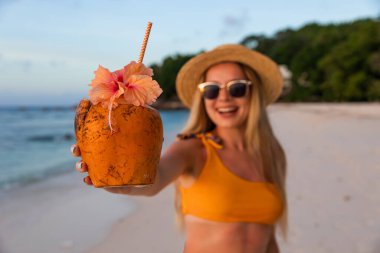 Mutlu kadın tropik sahilde hindistan cevizi içeceği tutuyor ve hava atıyor.