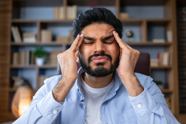 疲れ若い男インドのビジネスマンは重度の頭痛片頭痛を感じています 彼は机の上に座って目を閉じて頭を持っている — ストック写真