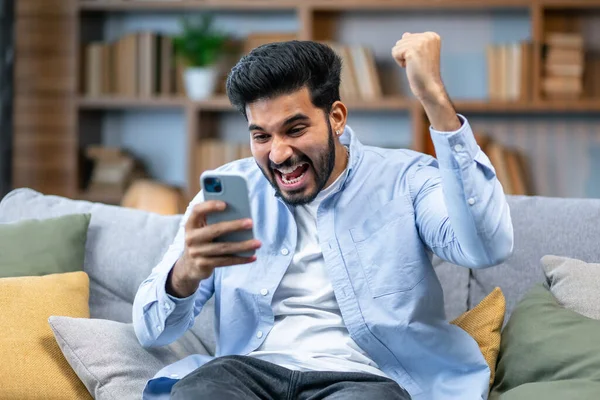 興奮した喜びのインド人男性勝者保持スマートフォン感陶酔とともにモバイルオンラインベット入札ゲーム勝利 幸せな恍惚アフリカ人男性携帯電話を見てお祝い読書良いニュースを受信 — ストック写真