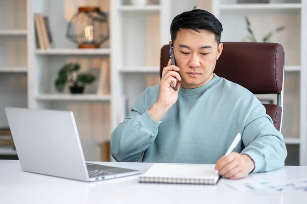 Asiático Homem Escrevendo Notas Fazer Telefonema Usando Laptop Casa — Fotografia de Stock