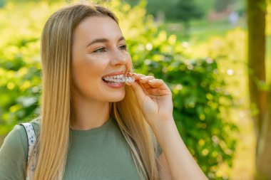 Gülümseyen kadın diş düzeltmesi için görünmez silikon dizgisini takıyor. Mobil ortodonti ve diş sağlığı konsepti.
