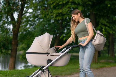 Doğum iznindeki bir kadın bebeğini bebek arabasıyla dışarı çıkarıyor. Anne ve bebek arabası dışarıda..
