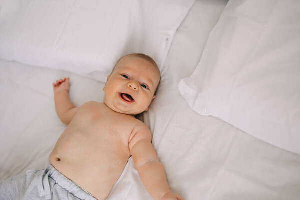 Happy newborn baby lying on white sheet