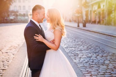 Yeni evliler kameraya bakar ve eski kasaba meydanına gülümser. Tramvay rayları ve eski fenerlerle dolu meydan.