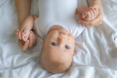 Beyaz yumuşak yatakta uzanan, uyuduktan sonra uyanıp anne eliyle oynayan güzel bir kız bebek görmek güzel. Evde yeni doğmuş bir çocuk