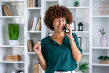 Afrikalı bir kadının kutlama görüntüsü, elinde akıllı telefon ve heyecandan tezahürat yapması, kazanması, cep telefonundan harika haberler alması. İnsanlar ve yaşam tarzı kavramı