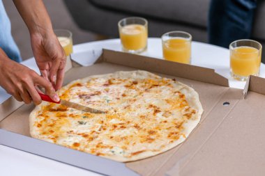 Kapatın peynirli pizzayı kadın el bıçağıyla dilimleyin taze meyve suyunun yanında küçük bir masada gözlüklü olarak durun..