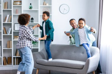 Mutlu bir aile, modern oturma odasında oğullarıyla eğlenceli bir oyun oynuyor. Sevimli çocukları olan genç bir anne ve baba hafta sonu evde eğleniyor..