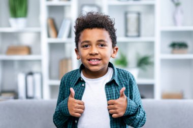 Güzel, sevimli, sevimli, çekici, genç ve neşeli çocuğun baş parmağını gösteren yakın plan portresi.