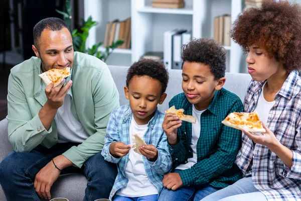 Family Eating Pizza At Home. african american family with two kids eat pizza. Mom, dad and sons enjoy time together.