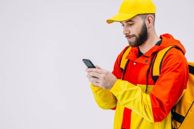 Elinde bir sırt çantası ve akıllı telefonu olan bir kurye. Sarı ceketli bir kurye emir beklerken sosyal medyayı kontrol ediyor..