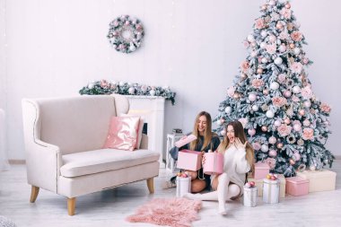 Gülümseyen genç kadınlar evdeki güzel Noel ağacının yanında bir hediye kutusu açıyor. Noel ve yeni yıl hediyeleri. Şömineli ve kanepeli beyaz oda..