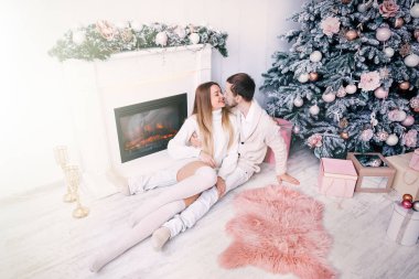 Sarılmalar, şöminenin yanında bir öpücük ve beyaz odada Noel ağacı. Birbirine aşık çiftler.