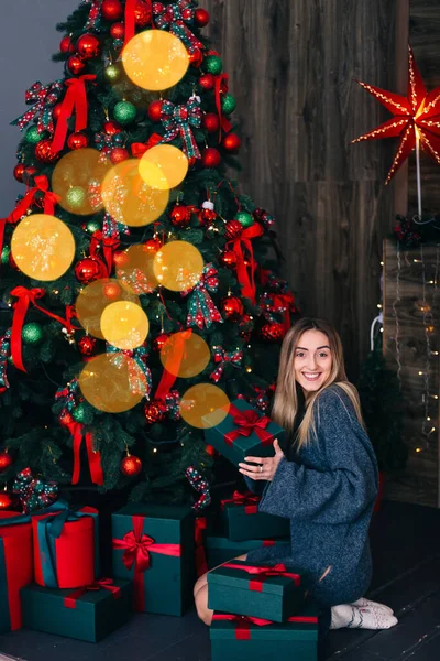 Girl Long Hair Gray Sweater Sits Christmas Tree Holds Gift — Stock Photo, Image
