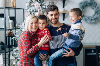 Anne, baba, Noel 'de evde havai fişeklerle poz veren iki oğul dekorasyonun arka planına karşı.