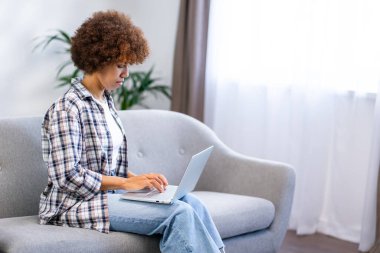 Güzel bir kadın dizüstü bilgisayarı tutuyor. Hafta sonu evde kanepeye otur.