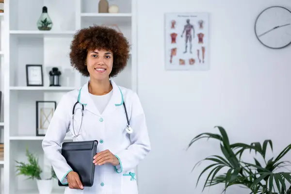 Female doctor in white medical gown with stethoscope standing with clipboard.