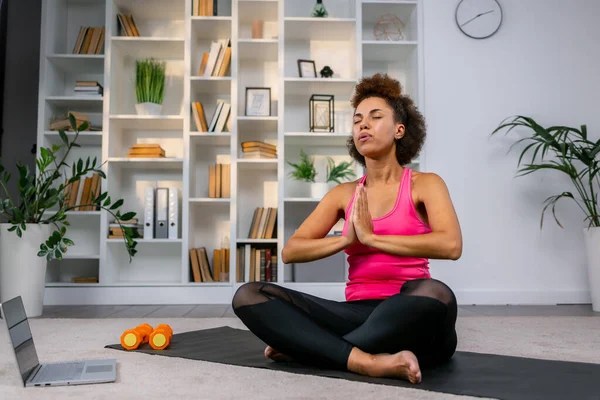 young lady practicing yoga at home, placing hands up in namaste gesture, meditating, copy space. Sporty flexible woman having yoga workout, living room interior