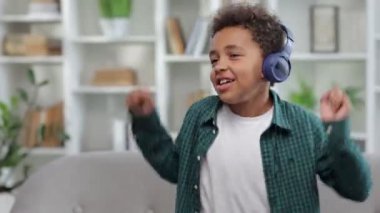 Brezilyalı etnik çocuk dans ediyor ve gülümsüyor. Rahatlıyor ve evde eğleniyor. Kulaklıkla müzik dinliyor.