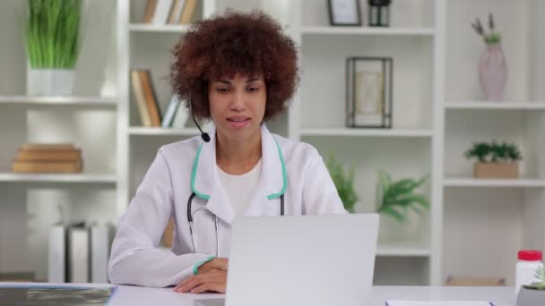 身穿白色医疗制服的年轻非洲裔美国女医生使用笔记本电脑 在诊所或医院的办公桌前与病人进行视频通话 咨询和治疗概念 — 图库视频影像