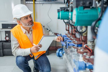 Koruyucu üniforma giyen Kafkas mühendisi ve fabrikadaki gaz boru tesisatı ve ekipmanlarını kontrol ediyor..