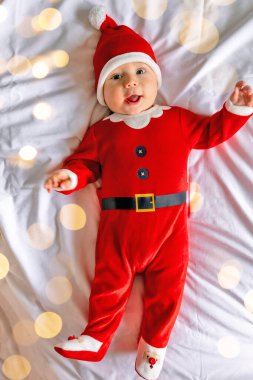 Noel Baba kostümü giymiş şirin bir erkek bebek yatakta yatıyor, mutlu bir çocuk Noel 'i ve evde yeni yılı kutluyor.