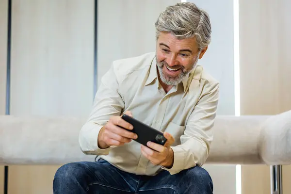 Carefree businessman playing funny online video game with smartphone enjoying mobile application in office. People and gaming concept.