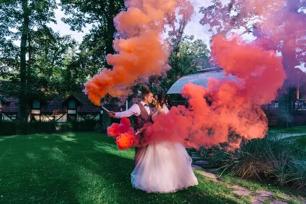 Bride and groom with red smoke bombs in summer park. Groom and bride with colored smoke on the background of the summer forest.
