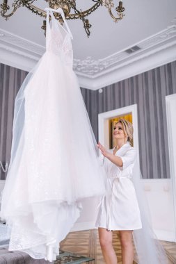 Güzel kız gelinliğine bakar, askıda asılı olan gelinliğine.